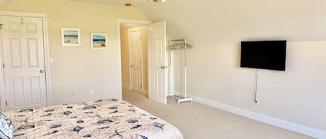 Une chambre à coucher comprenant un lit, un ventilateur de plafond, un téléviseur et un couloir menant à une autre pièce.
