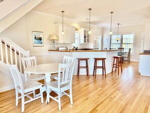 A kitchen with a central island, white cabinetry, and a dining area with white chairs. - Old Bay Watch: 3BR 2.5BA, Walk to Beach, Boat Parking, Sleeps 6 (Oak Island)