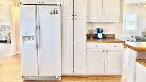 Una cocina con muebles blancos, un refrigerador, una cafetera y un dispensador de agua.