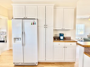 Eine Küche mit weißen Schränken, einem Kühlschrank, einer Kaffeemaschine und einem Wasserspender.
