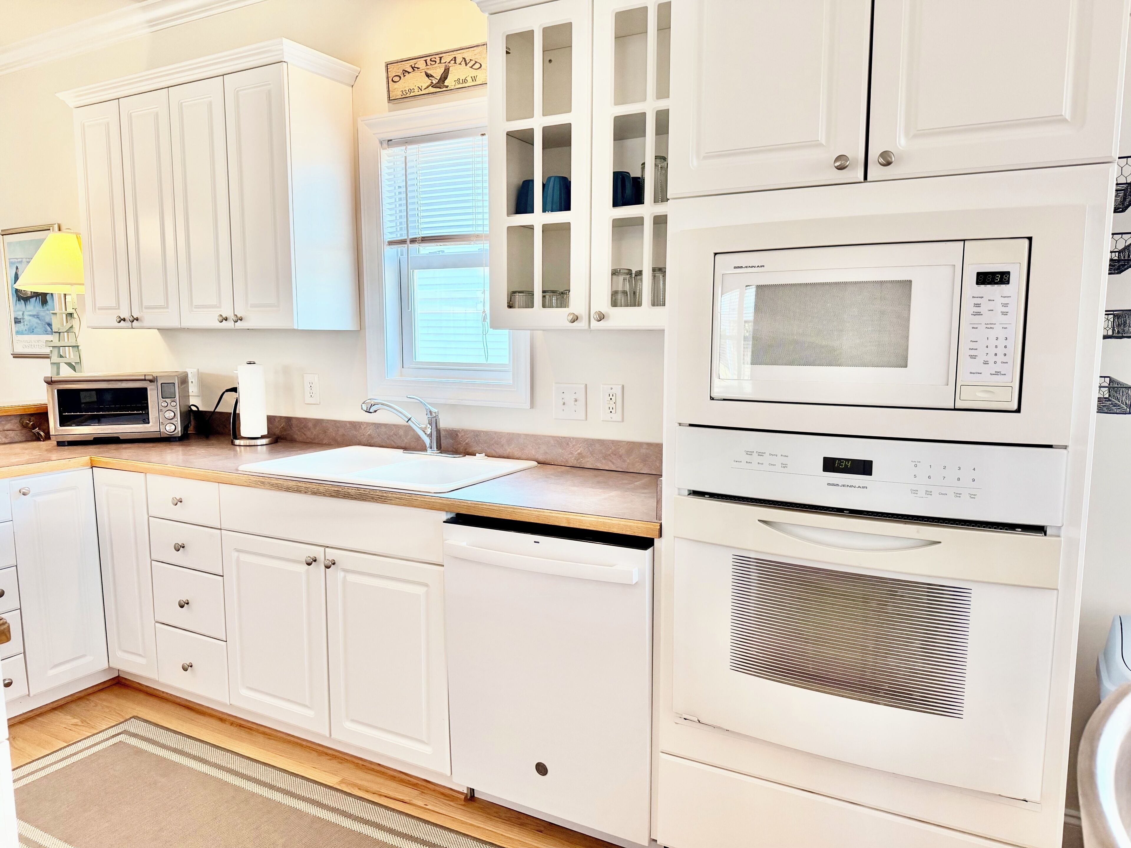 A kitchen with white cabinetry, a built-in microwave, a dishwasher, and a window with blinds.