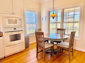 A kitchen with white appliances, a dining table with chairs, and large windows with blinds. - Old Bay Watch: 3BR 2.5BA, Walk to Beach, Boat Parking, Sleeps 6 (Oak Island)