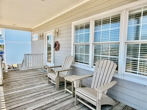 Eine hölzerne Veranda mit zwei Adirondack-Stühlen und einer Bank, eine weiße Tür und ein Fenster mit Jalousien.