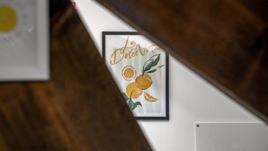 En indrammet kunstplakat med teksten 'Le Dolce Vita' og illustrationer af appelsiner på en væg.