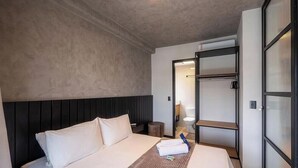 Ein Hotelzimmer mit einem Bett, einem Nachttisch, einem Kleiderschrank und einem durchgegangenen Tür angedeuteten Badezimmer.