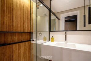 A modern bathroom with a wooden vanity, a glass shower enclosure, and a large mirror. - Apt. in Condo. w/ Pool & Garage Pea0410 (Florianópolis)
