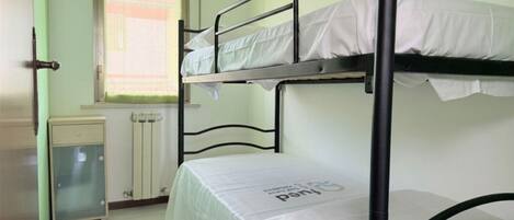 A bunk bed room with a radiator, a small cabinet, and a window with blinds.