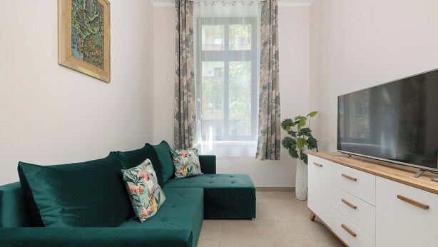 A modern living room with a green sofa, a flat-screen TV, and a window with curtains. - Cosy Apartment for 4 People | Coffee Machine (Bielsko-Biała)