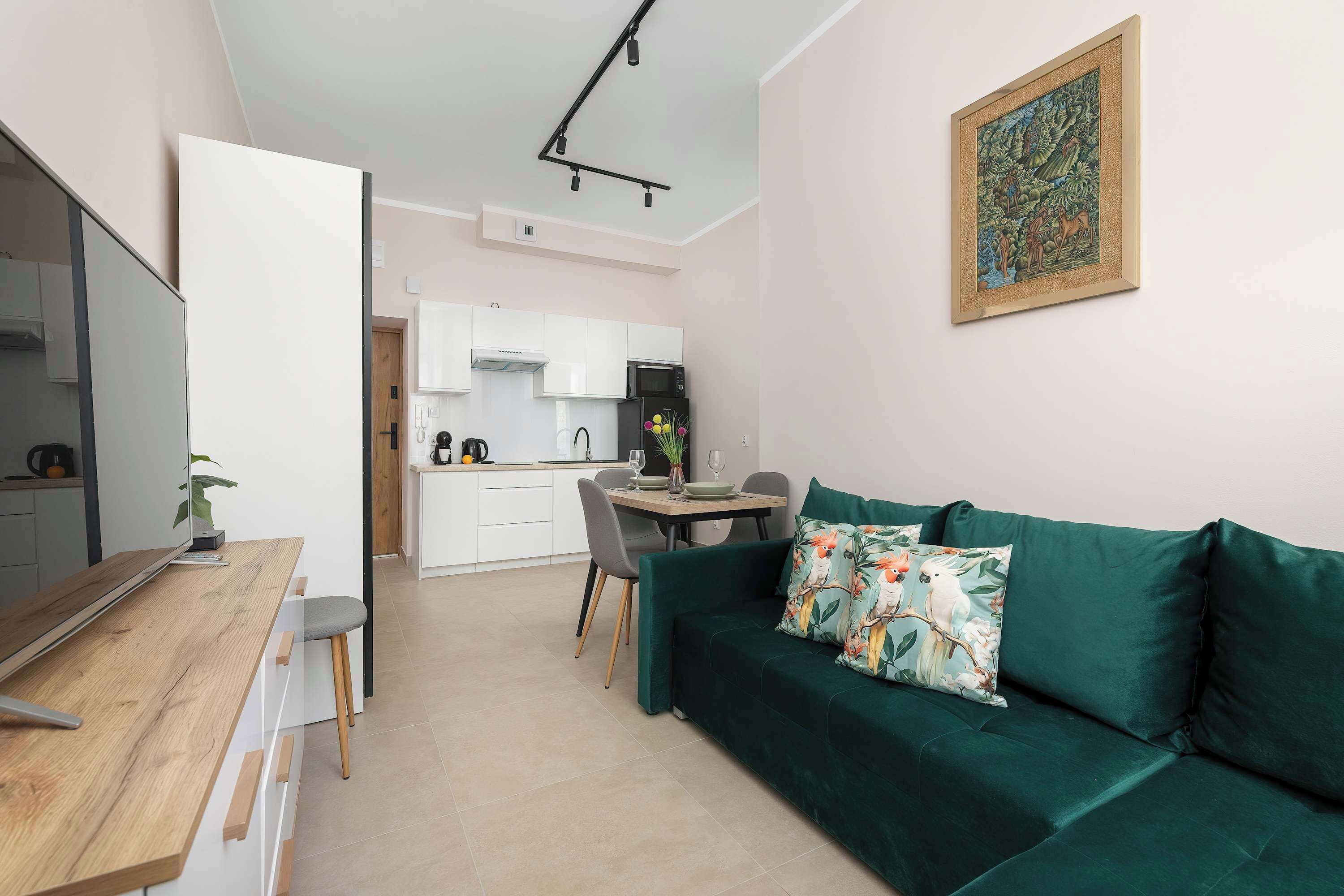 Ein moderner Wohnraum mit Essbereich, Küchenzeile und einem grünen Sofa mit floralen Kissen.