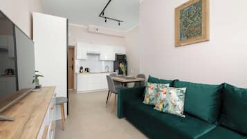 Un espace de vie moderne comprenant un coin repas, une kitchenette et un canapé vert agrémenté de coussins à motifs floraux.