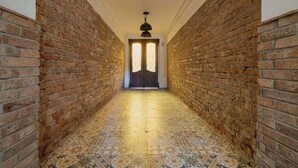 A hallway with brick walls and patterned floor tiles leading to a door with a decorative light fixture above. - Cosy Apartment for 4 People | Coffee Machine (Bielsko-Biała)