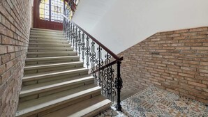 Un escalier avec un mur en briques, une porte en bois ornée d’un vitrail et des carreaux de sol à motifs.