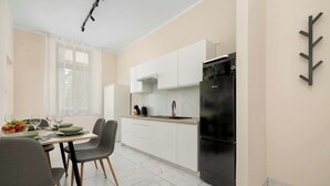 Une cuisine moderne avec des meubles blancs, un réfrigérateur noir et un coin repas avec une table mise pour deux personnes.