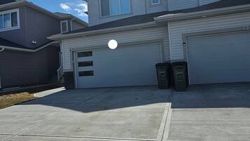 Un garage attenant à une maison, avec un ciel dégagé, une allée et deux poubelles.