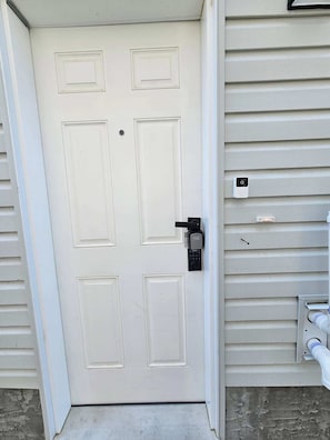 Uma porta branca com maçaneta preta e fechadura, embutida numa casa com revestimento.