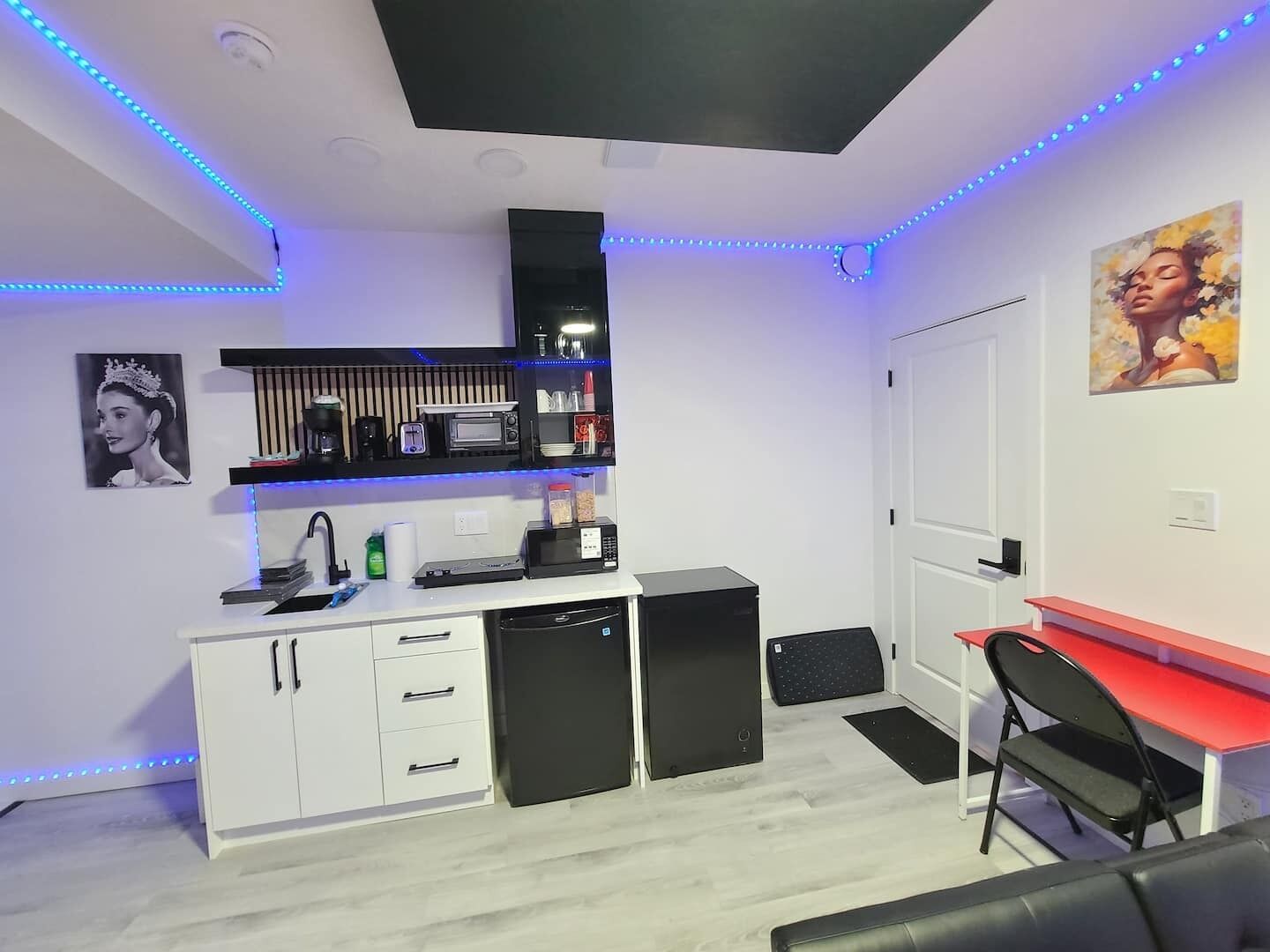 A compact room with a kitchenette, a desk, and a chair.