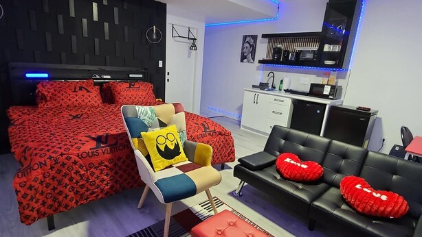 A modern living room with a sofa, ottoman, and a chair with a cushion. There is a kitchen area with a microwave and cabinets. - SwitHome Cher Cozy Studio: Pond View, Near YEG Airport (Edmonton)