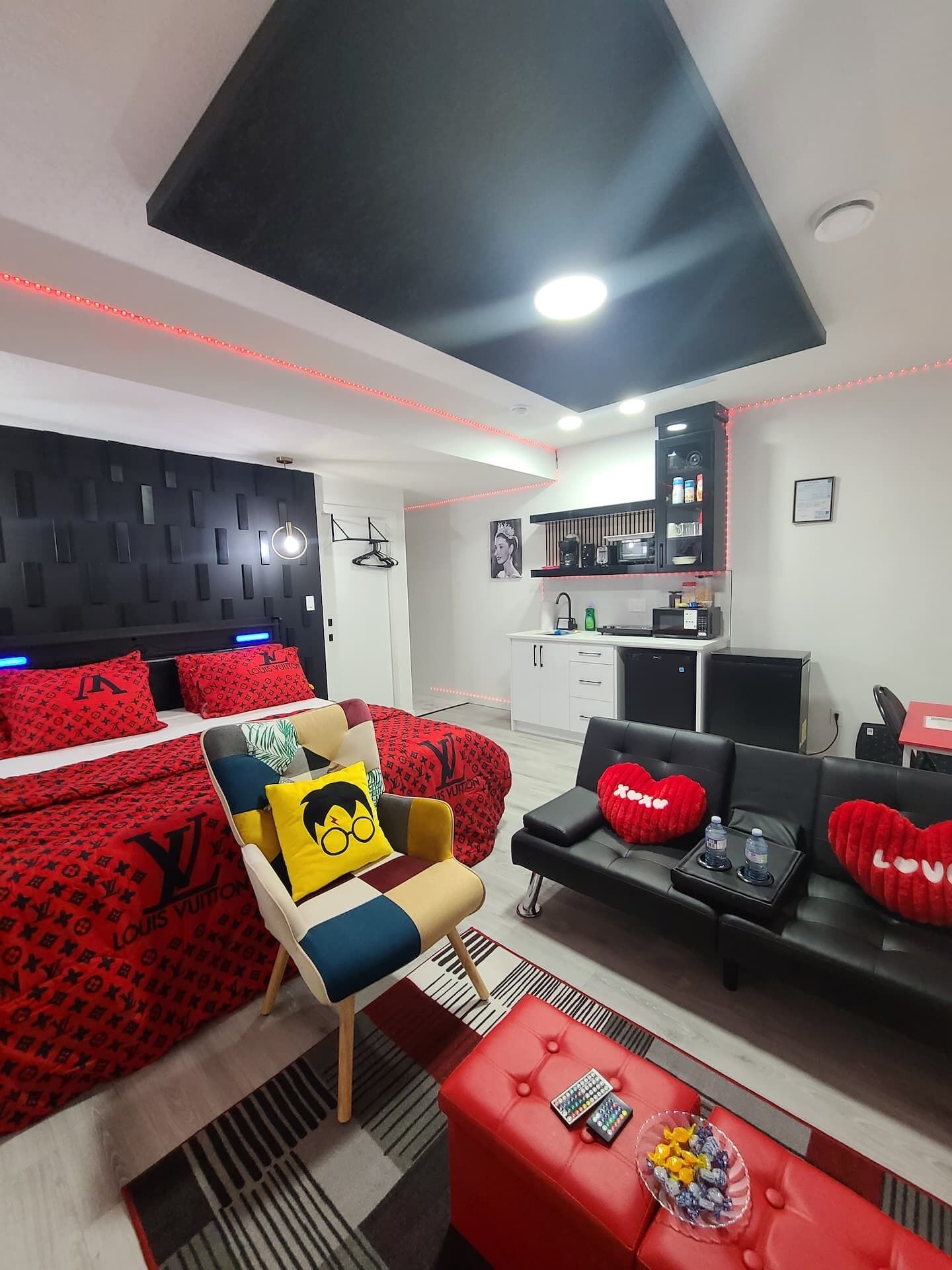 A modern bedroom with a bed, a sofa, a chair, and a kitchenette.