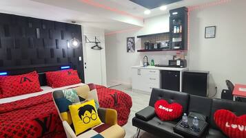 A modern bedroom with a bed, a sofa, a chair, and a kitchenette.