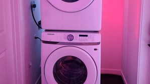 A stacked washer and dryer unit in a room with pink lighting. - SwitHome Cher Cozy Studio: Pond View, Near YEG Airport (Edmonton)