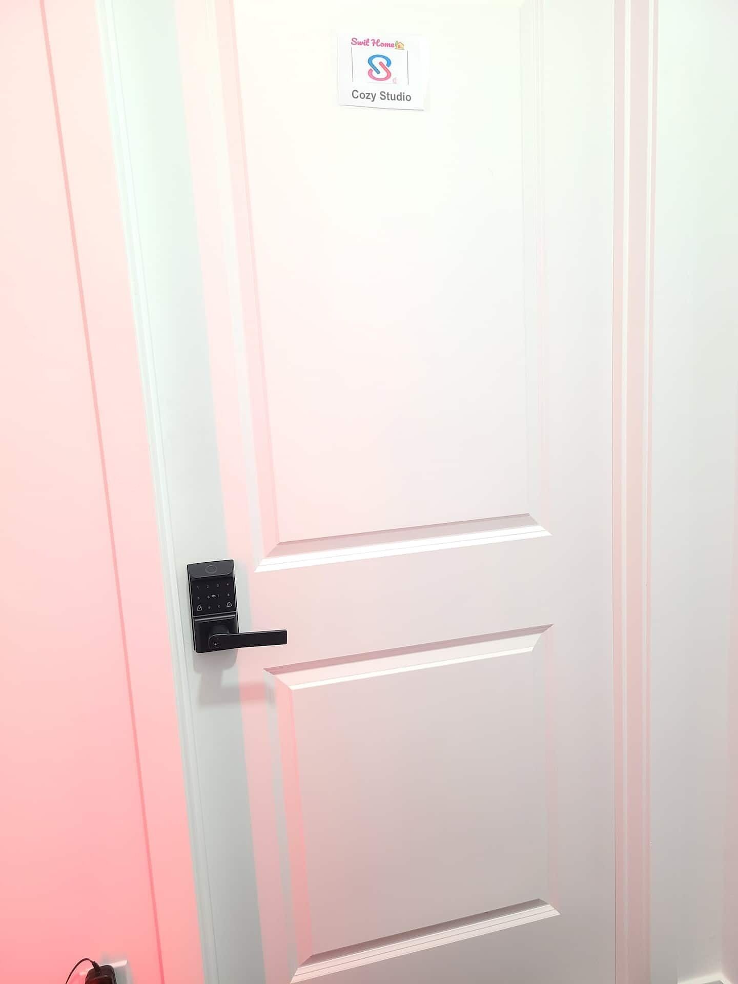 En hvid dør med Swell Home Cozy Studio logo, et sort håndtag og en nøglehul.