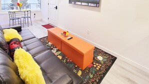 Moderni olohuone, jossa on musta nahkasohva, oranssi rahi ja seinälle asennettu litteänäyttöinen televisio.