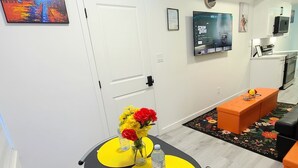 Moderni olohuone, jossa on ruokailutila, seinälle asennettu taulutelevisio ja taustalla keittiö.