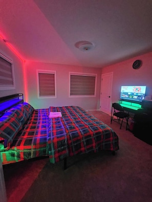 Um quarto com uma cama, uma escrivaninha com computador e uma televisão.