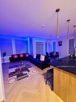 Ein modernes Wohnzimmer mit einer schwarzen Couch, einem Essbereich und einer Küchenzeile.