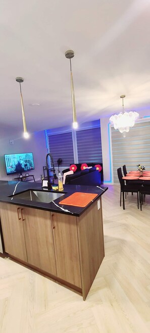 Eine moderne Küche mit einer zentralen Kochinsel, einem Essbereich mit Tisch und Stühlen sowie einem Wohnbereich mit einer Couch und einem Fernseher.