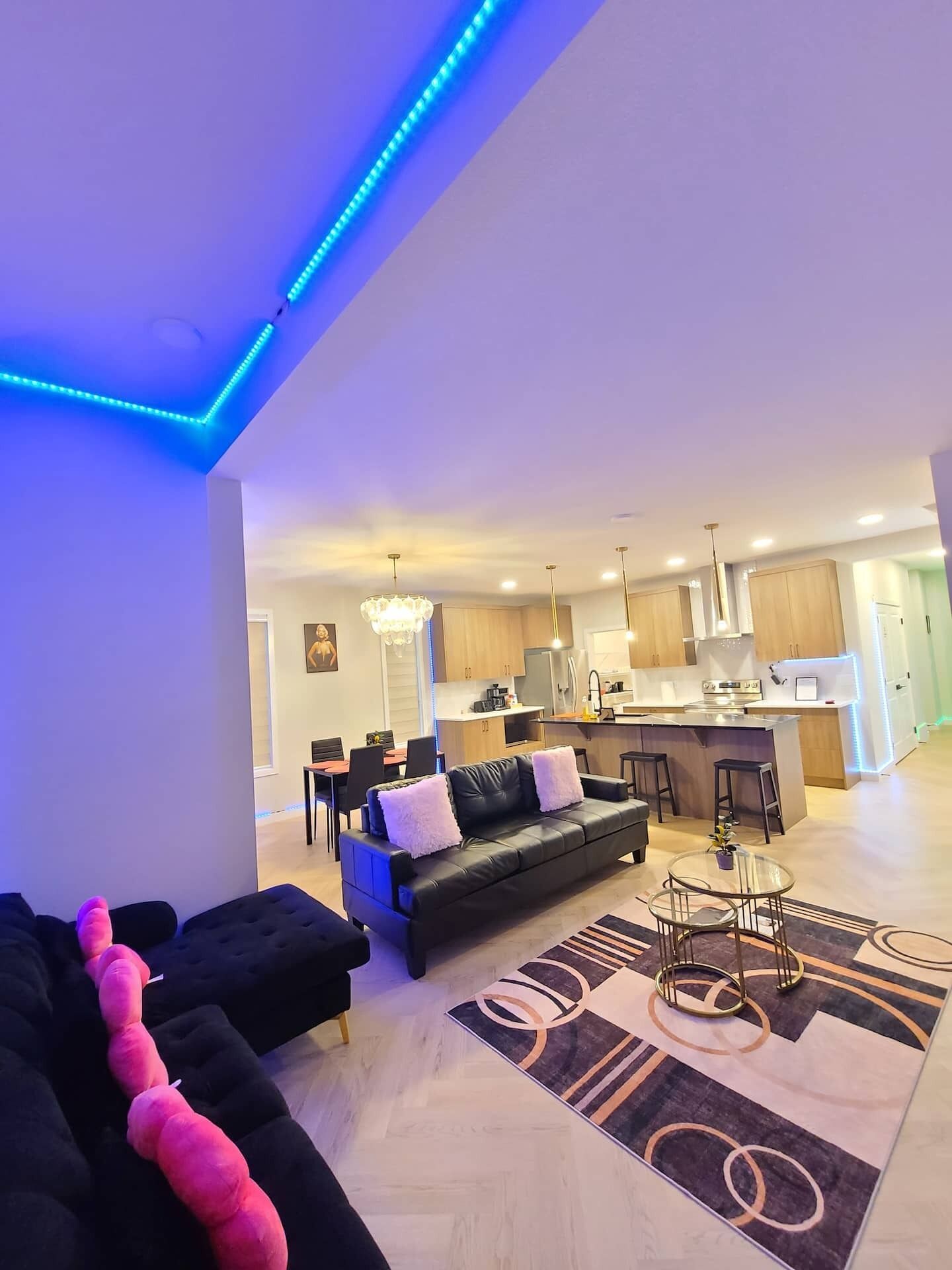 Ein modernes Wohnzimmer mit einer schwarzen Couch, einem Essbereich und einer Küche mit Holzausstattung.