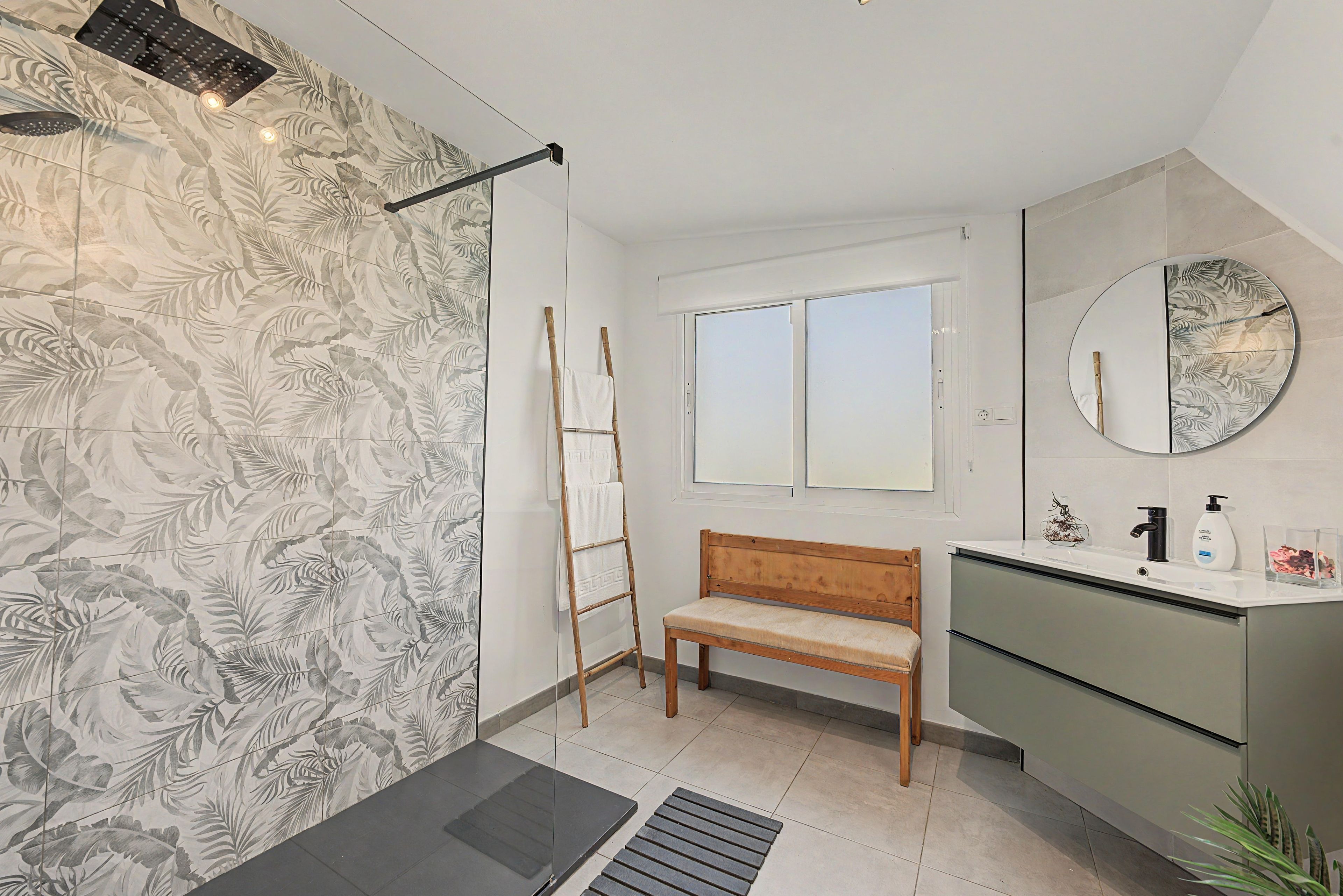 Un baño con ducha, un banco, un tocador con espejo y una ventana.
