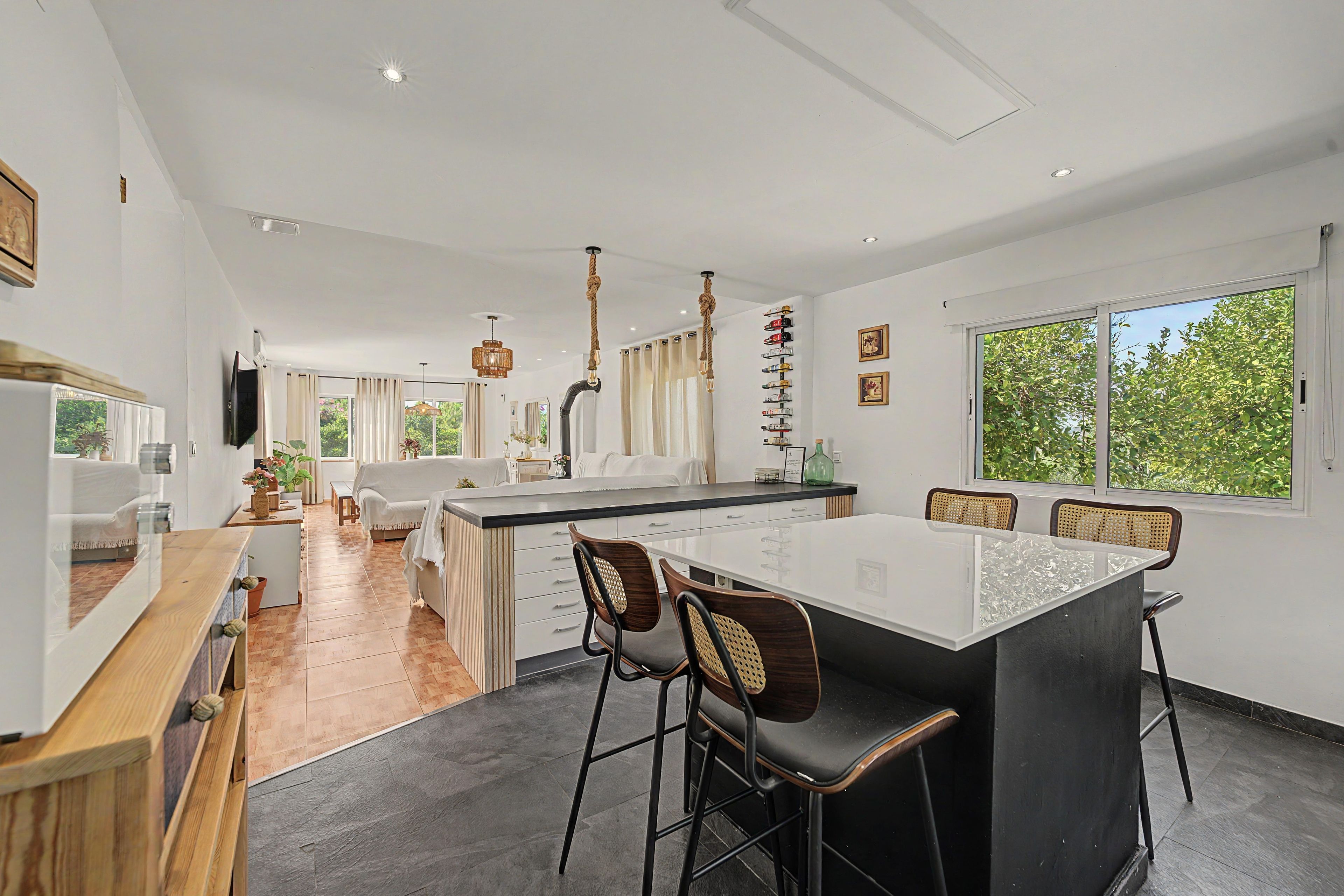 Een moderne keuken met een centraal eiland, barkrukken en een eethoek met een groot raam.