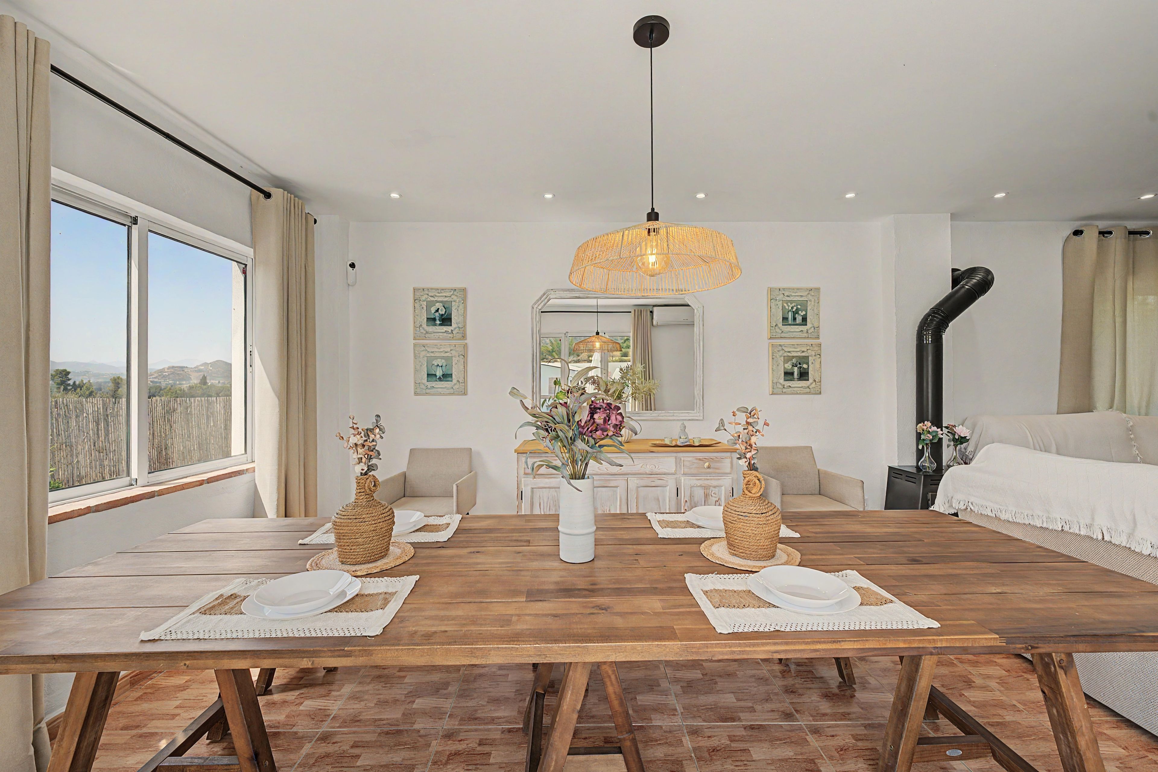 Un comedor con una mesa de madera dispuesta para dos, una lámpara colgante y vistas al exterior a través de amplios ventanales.