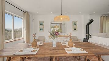 Un comedor con una mesa de madera dispuesta para dos, una lámpara colgante y vistas al exterior a través de amplios ventanales.