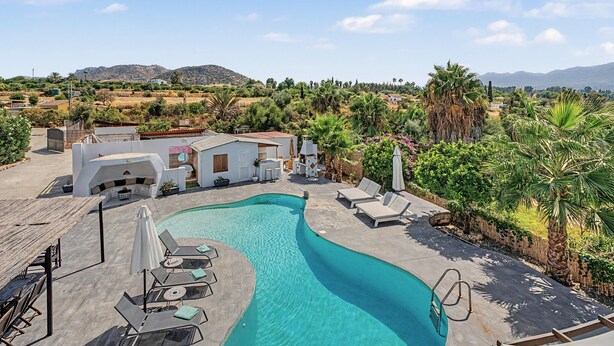 Un área de piscina con sillones de descanso y una casa al fondo.