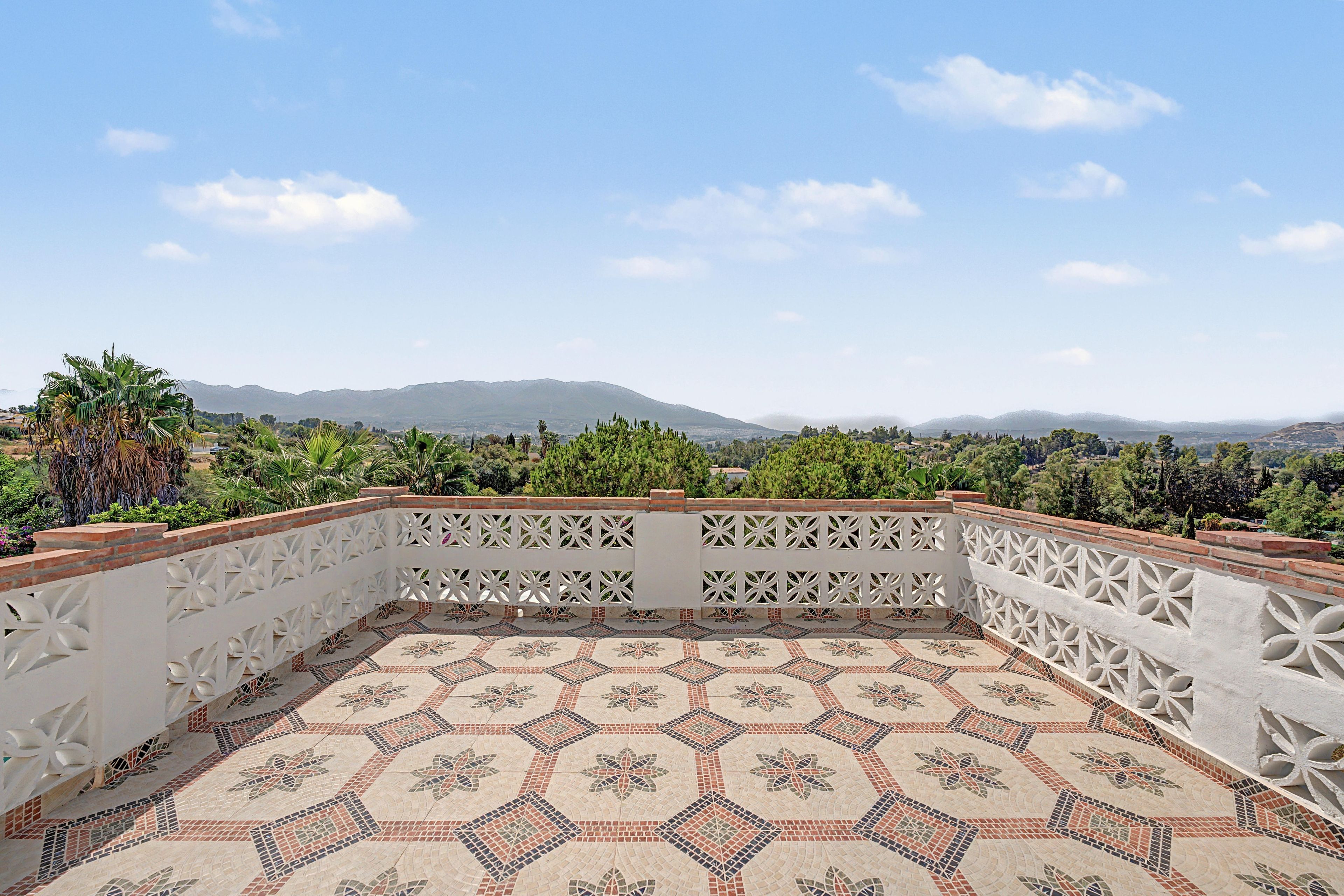 Une terrasse sur le toit, dotée d’un sol à motifs, d’une balustrade blanche décorative et offrant une vue sur les montagnes lointaines.