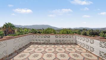 Une terrasse sur le toit, dotée d’un sol à motifs, d’une balustrade blanche décorative et offrant une vue sur les montagnes lointaines.