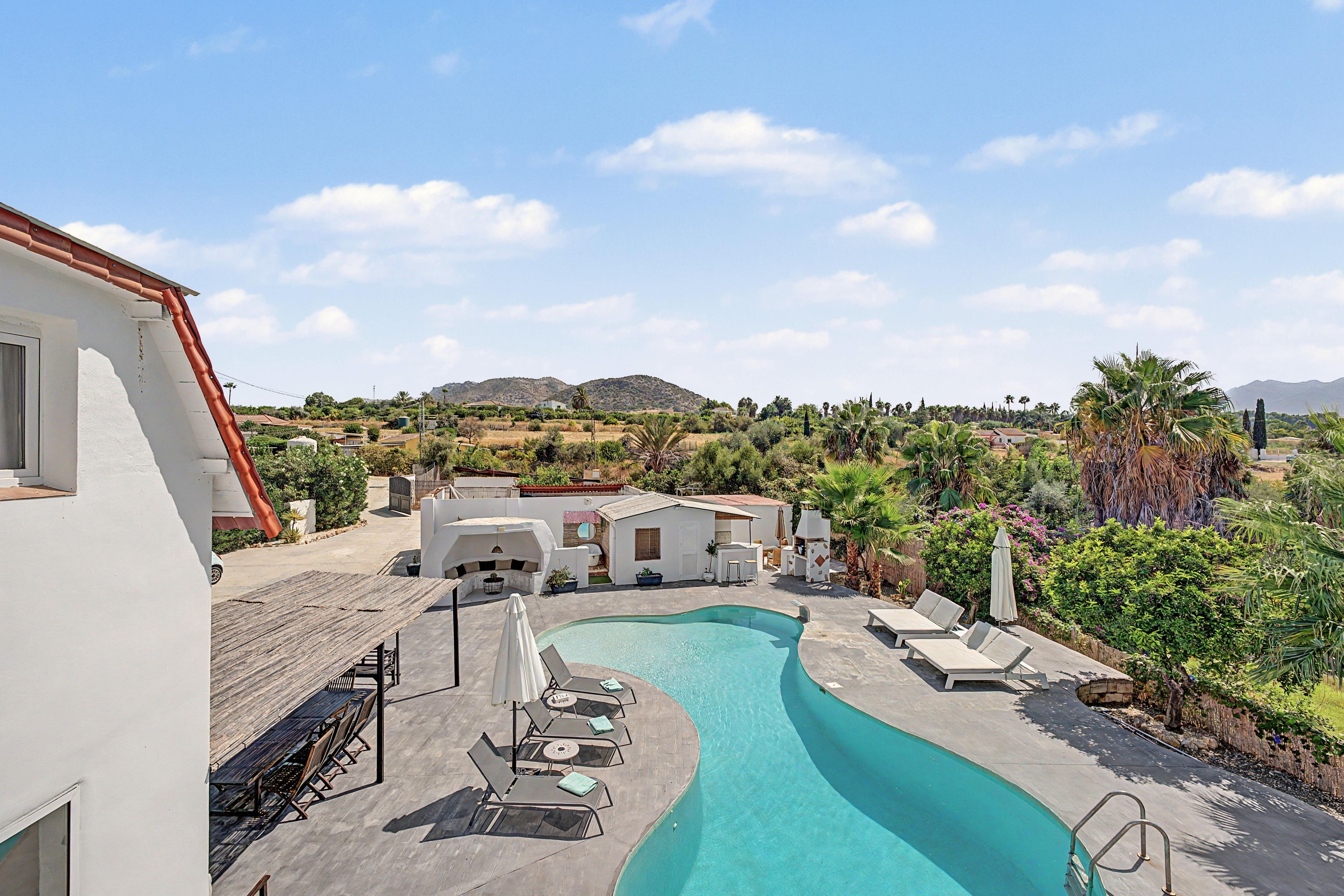 A swimming pool with lounge chairs and a view of a residential area with houses and mountains in the background.