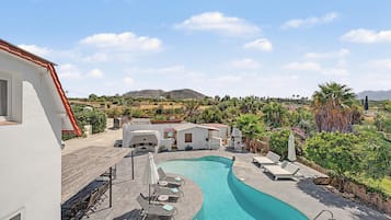 A swimming pool with lounge chairs and a view of a residential area with houses and mountains in the background.