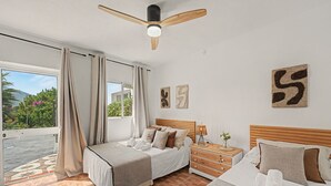 Un dormitorio con cama, mesita de noche, lámpara y vistas al exterior.
