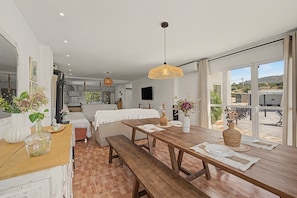 A spacious room with a wooden dining table, a sofa, and a large window offering a view of the outdoors. - Villa 'Finca Raziel' with Pool, Mountain Views, and Wi-Fi (Cártama)