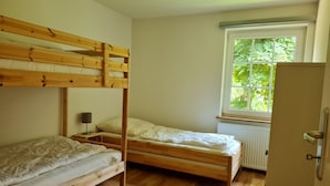 Une chambre avec deux lits superposés, un radiateur, une fenêtre donnant sur un espace verdoyant et une porte.