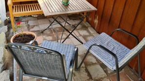 Une terrasse avec un banc en bois, une table et deux chaises.