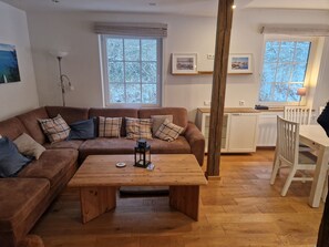 Un salon chaleureux avec un canapé marron, une table basse en bois et un coin repas comprenant une table et des chaises blanches.