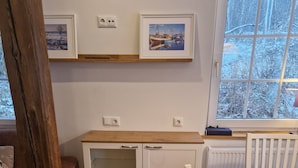 Une cuisine de taille réduite, dotée de meubles en bois, d’un plan de travail blanc et d’une fenêtre donnant sur la verdure.