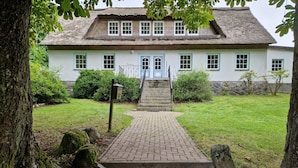 Un bâtiment traditionnel avec un toit de chaume, un escalier en pierre menant à une porte bleue et un chemin pavé.