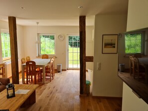 Une pièce spacieuse avec un plancher en bois, un coin repas comprenant des chaises et une table, une grande fenêtre donnant sur un paysage verdoyant et une horloge au mur.