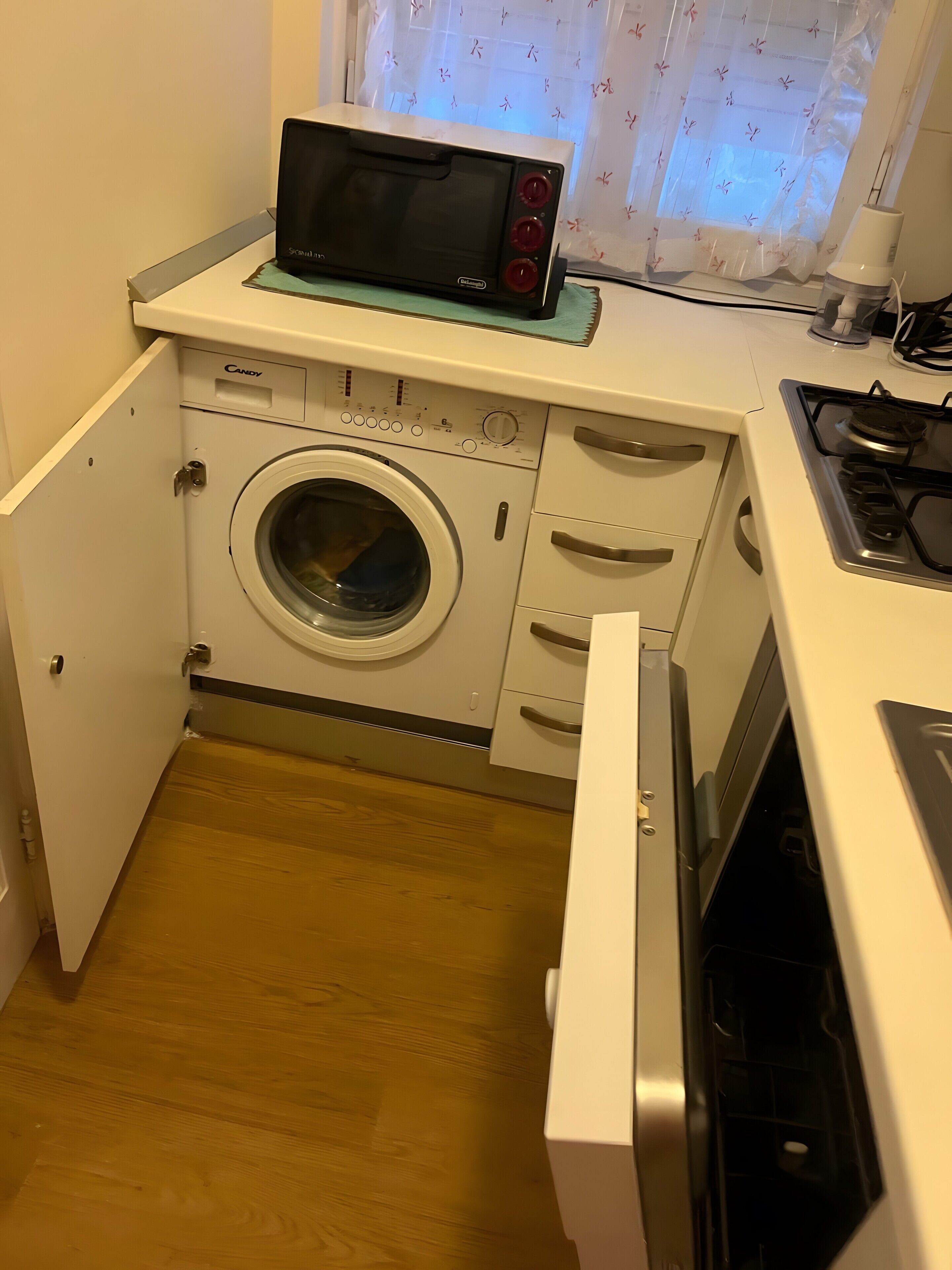 A compact kitchen with a microwave, washing machine, and a stove.