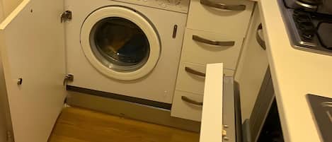 A compact kitchen with a microwave, washing machine, and a stove.